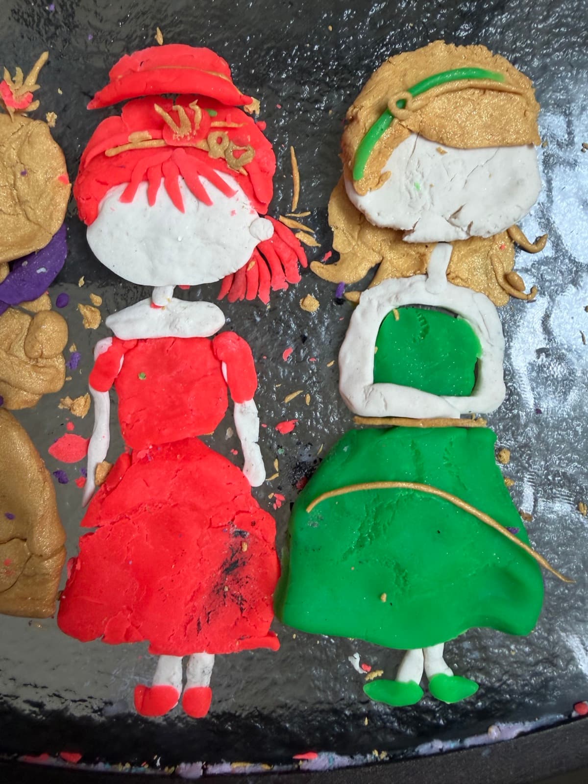 Two clay figures in red and green dresses standing side by side