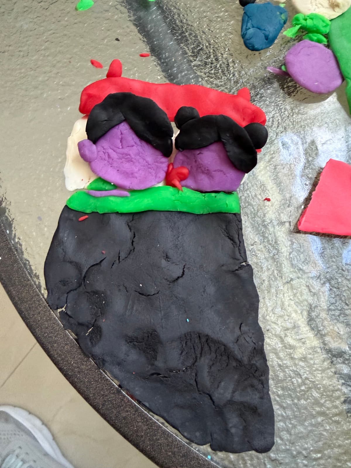 Clay artwork of two figures with dark hair and a black cape
